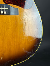 Close-up of a sunburst electric guitar body showing the glossy wood finish, scratches, and wear on the upper bout area, with part of the pickguard and strings visible.