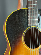 Close-up of an acoustic guitar body showing the dark black fingerboard with a cracked finish, the yellow binding, and the warm brown wood grain of the soundboard.