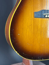 Close-up of the lower bout corner of a sunburst acoustic guitar, showing the amber-brown wood finish, yellow binding, and part of the black bridge.