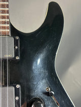 Close-up of a black electric guitar with visible wear on the body.