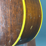 Close-up of a dark brown wooden guitar body with a bright yellow binding edge, showing visible wear, scratches, and scuffs on the wood finish.