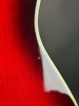 Close-up of a glossy red electric guitar body showing the wood grain finish and a white binding edge against a dark background.
