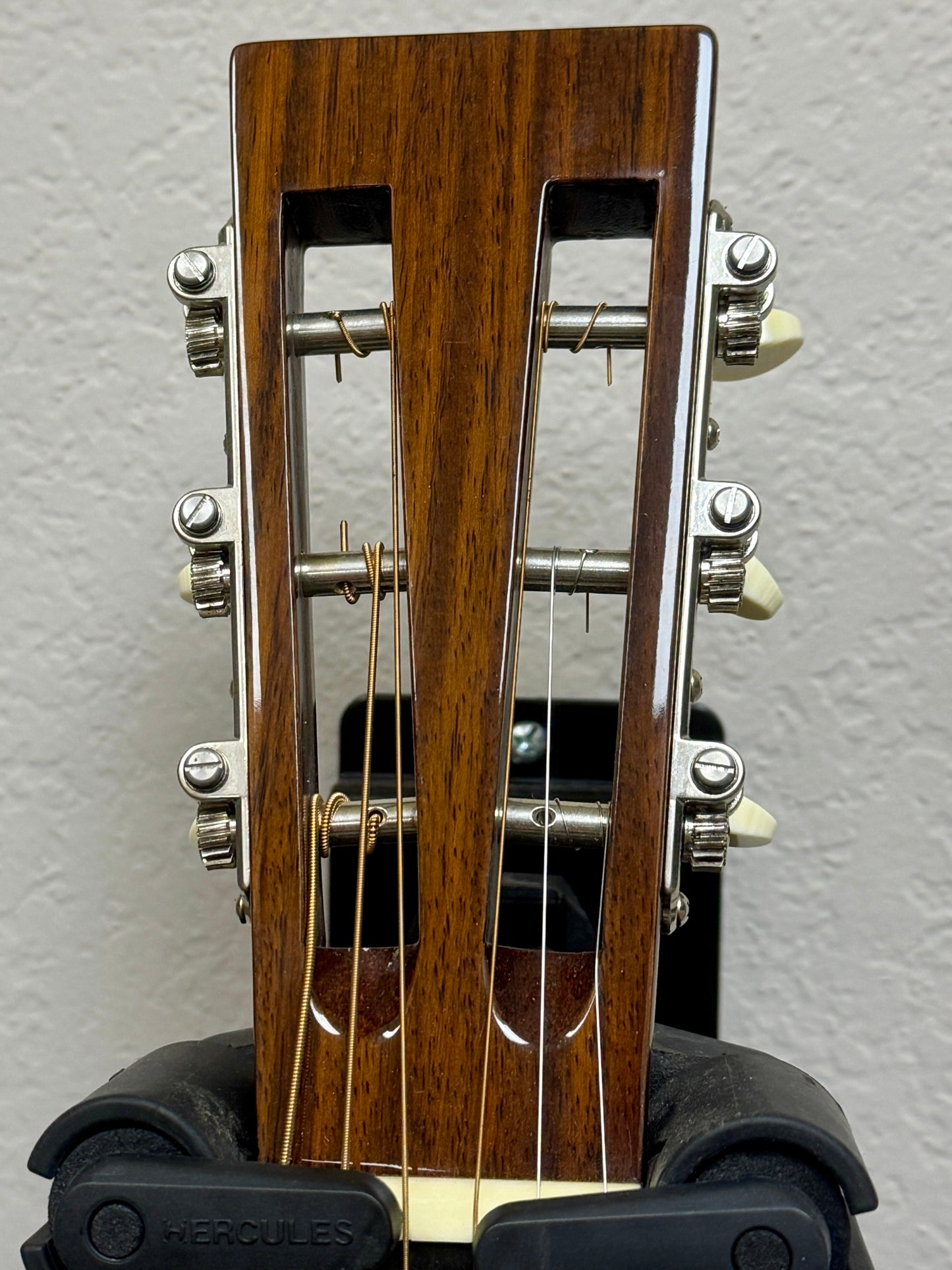 Close-up of a guitar headstock with wooden finish and metal tuning pegs on a gray background.