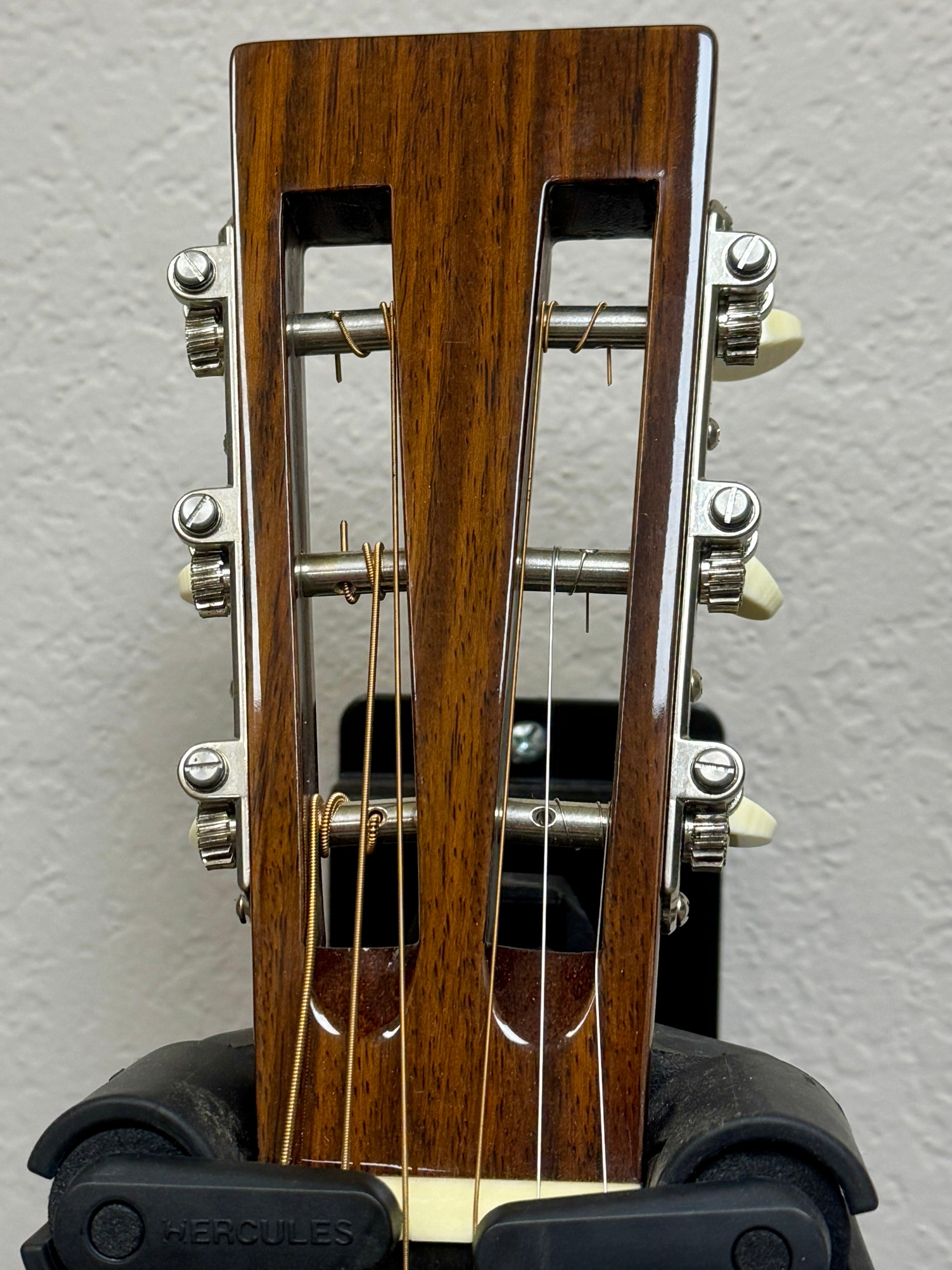 Close-up of a guitar headstock with wooden finish and metal tuning pegs on a gray background.