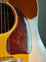 Close-up of an acoustic guitar body showing the glossy brown pickguard, sound hole, and natural wood grain finish.