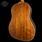 Close-up of the back of an acoustic guitar showing a rich, warm brown wood grain finish with a white binding edge, set against a solid black background.