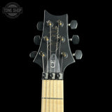 Close-up of the headstock and upper neck of a black electric guitar against a black background, with a Tone Shop watermark in the top left corner.