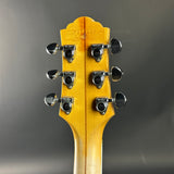 Close-up of a guitar headstock with tuning pegs on a gray background