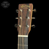 Close-up of the headstock of a Martin & Co acoustic guitar against a black background, showing the brand name in gold script, six tuning pegs, and part of the dark wood fretboard.