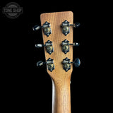Close-up of the headstock of a wooden acoustic guitar against a solid black background, featuring six tuning pegs with decorative metal caps and a Tone Shop watermark in the upper left corner.