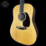 A natural wood acoustic guitar shown from a three-quarters angle against a solid black background, with a Tone Shop watermark in the upper left corner.