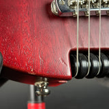 Close-up of a red electric guitar body near the bridge and strings, showing the wood grain, hardware, and black string trees against a dark background.