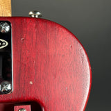 Close-up of a red electric guitar body showing the wood grain finish, chrome hardware, and part of the headstock against a dark gray background.