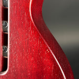 Close-up detail of a red electric guitar body showing the wood grain finish, edge contour, and part of the pickup area against a dark gray background.