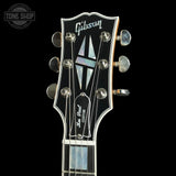 Close-up of the headstock of a Gibson Lark Bay Custom acoustic guitar against a black background, featuring mother-of-pearl inlays and silver tuning pegs.