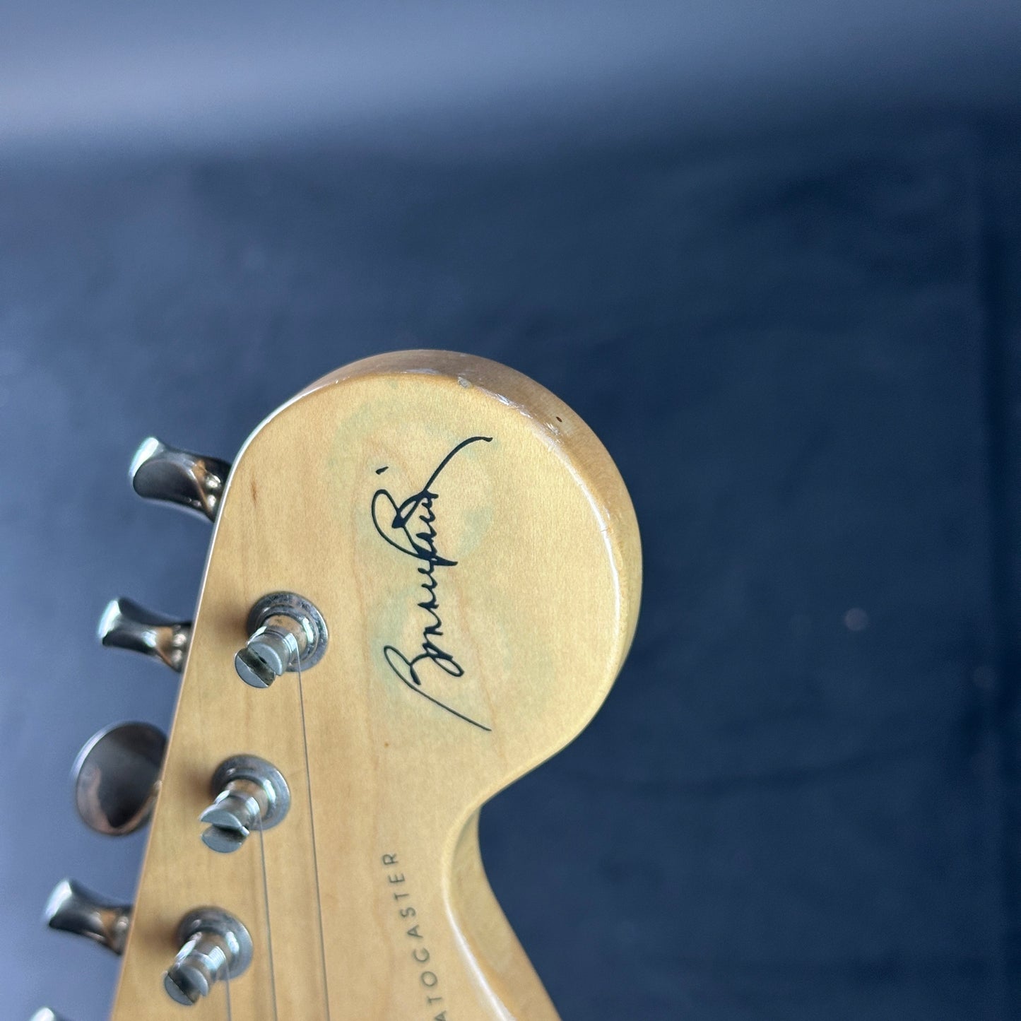 Close-up of a guitar headstock with a brand logo on a dark background