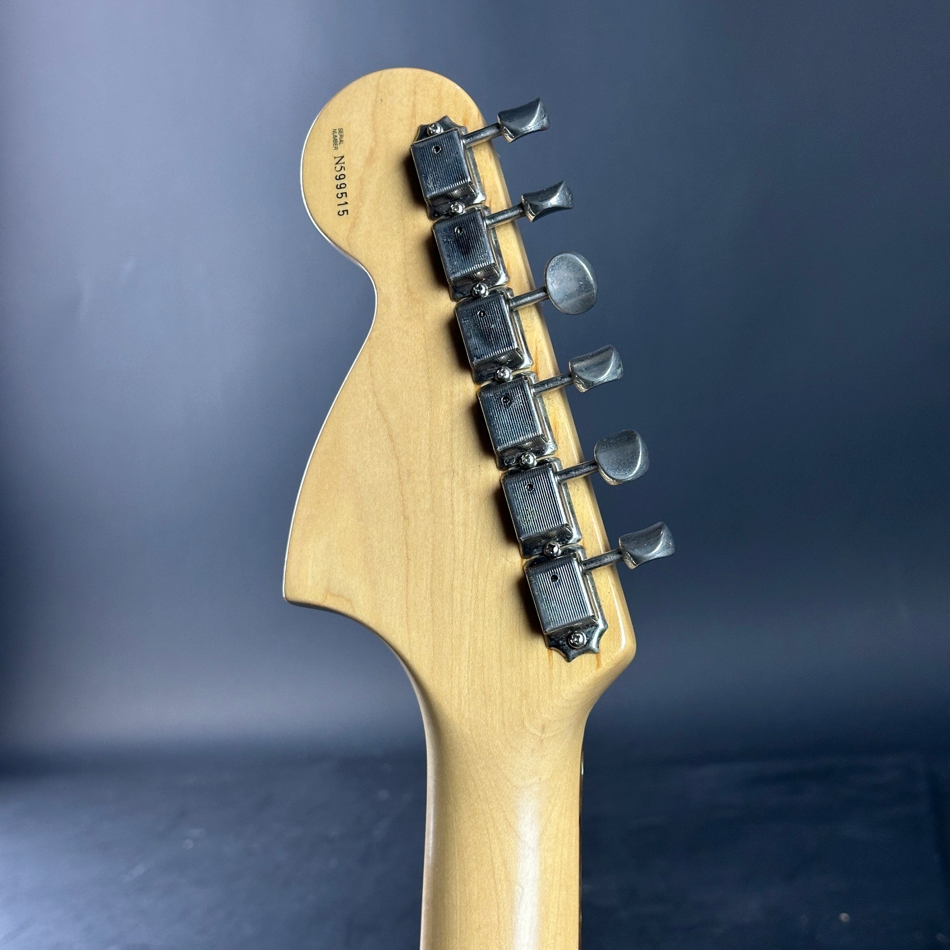 Close-up of a guitar neck with tuning pegs against a dark background