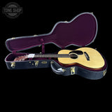 Acoustic guitar in an open case with a visible brand logo on a black background