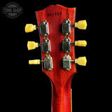 Close-up of the headstock of a red electric guitar against a black background, showing six yellow tuning pegs and silver tuning machines. A Tone Shop watermark is visible in the top left corner.