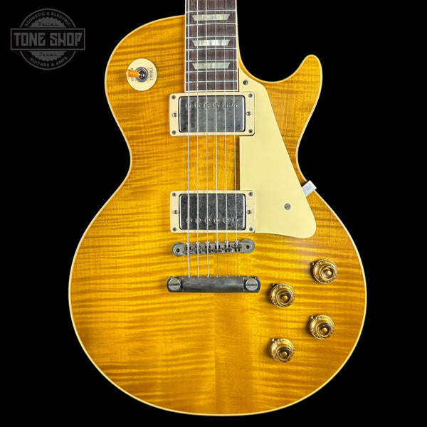 A close-up of a Gibson Les Paul Custom electric guitar with a vibrant flamed maple top in a golden yellow finish, featuring a cream pickguard and gold hardware, set against a solid black background.