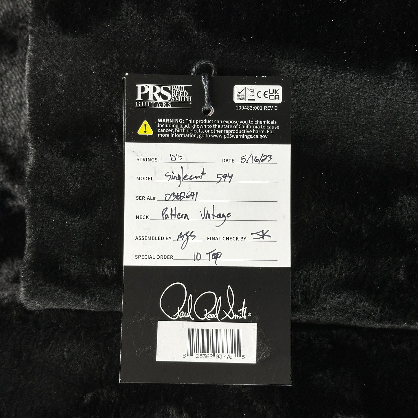 Close-up of a guitar label with branding and product details on a dark textured background