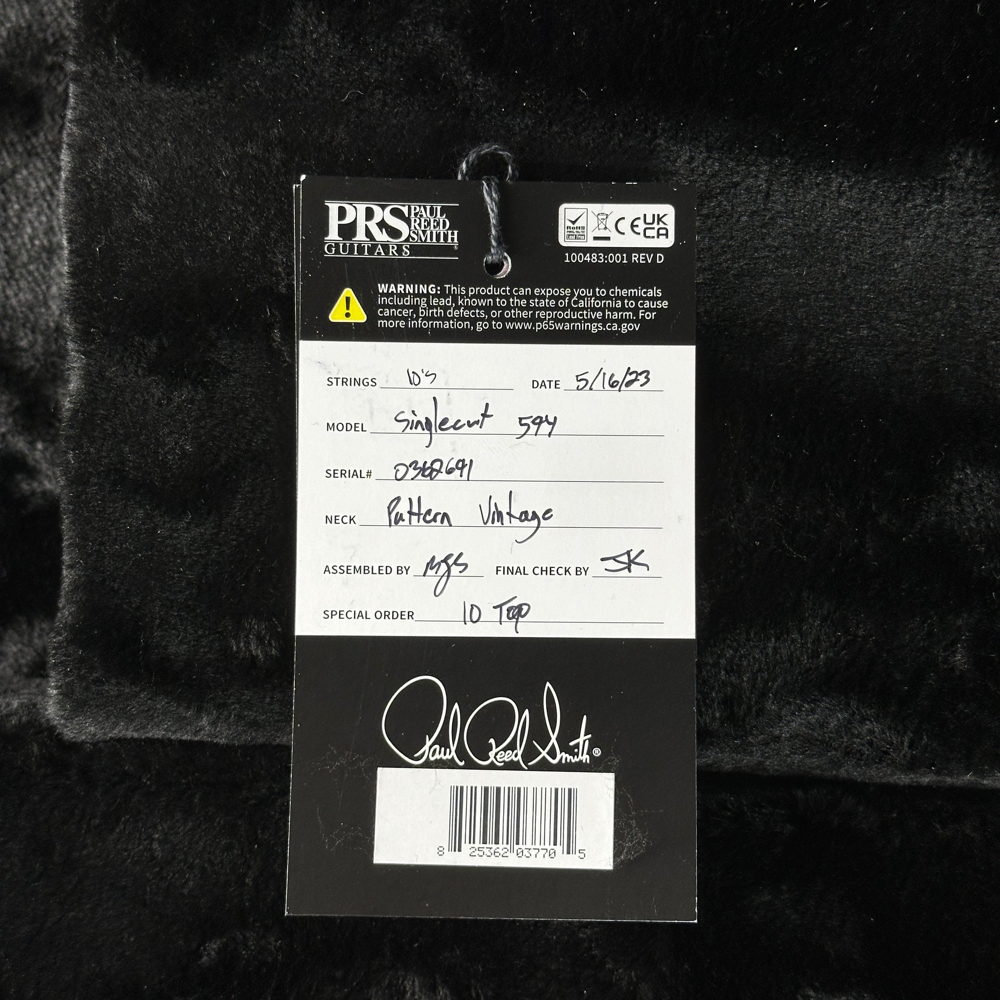 Close-up of a guitar label with branding and product details on a dark textured background