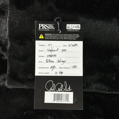 Close-up of a guitar label with branding and product details on a dark textured background