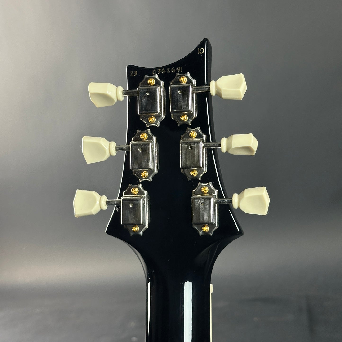 Close-up of a guitar headstock with tuning pegs on a gray background