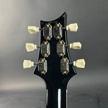 Close-up of a guitar headstock with tuning pegs on a gray background