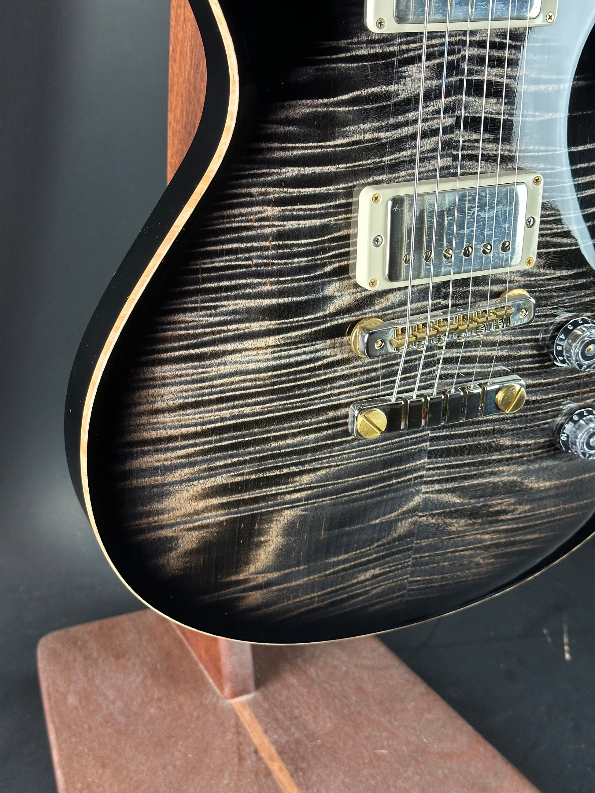 Close-up of a black electric guitar with a wood grain finish on a dark surface.