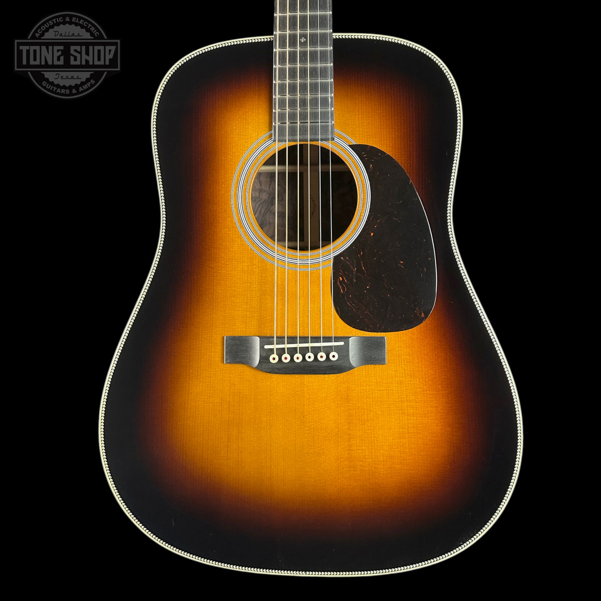 A classic acoustic guitar with a sunburst finish, featuring a warm orange and brown center fading to black around the edges, shown against a solid black background.