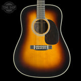 A classic acoustic guitar with a sunburst finish, featuring a warm orange and brown center fading to black around the edges, shown against a solid black background.