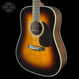 A classic acoustic guitar with a natural sunburst finish, dark wood sides, and white binding, shown against a solid black background with a Tone Shop watermark in the top-left corner.