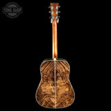 A double-cutaway acoustic guitar shown from the back, featuring a highly figured wood backplate and a matching wood neck, set against a solid black background with a Tone Shop watermark in the top-left corner.