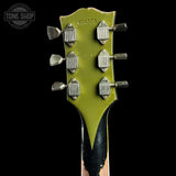 Close-up of a guitar headstock with a distressed olive green finish, six silver tuning pegs, and a black-and-brown wood neck visible against a black background. A Tone Shop watermark is in the upper left corner.