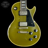 A vintage-style electric guitar with a distressed olive green finish, black pickguard, and chrome hardware, shown against a solid black background with a Tone Shop watermark in the top left corner.