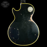 The back of a black Gibson electric guitar with a yellow binding edge, showing heavy wear, scratches, and a worn 'Gibson' logo patch on the upper right side. A 'Tone Shop' store watermark is visible in the top-left corner.