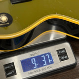 A close-up of a digital kitchen scale displaying 9.37 oz, with a green and black electric guitar resting on top of the scale.