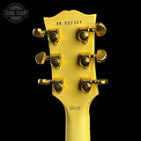 Close-up of the headstock of a yellow Gibson electric guitar against a black background, showing six gold tuning pegs and model number CS 502361.