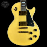 A close-up of a yellow Gibson Les Paul Custom electric guitar against a solid black background, showing the body, pickups, and control knobs.