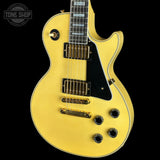 A gold-finish electric guitar with a black pickguard and gold hardware, shown against a solid black background. A 'TONE SHOP' watermark is visible in the top left corner.