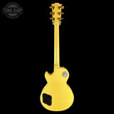 A yellow electric guitar shown from the back against a solid black background, featuring a glossy finish, gold tuning pegs, and a circular 'Tone Shop' watermark in the upper left corner.