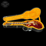 A red electric guitar inside an open black hard case with a bright yellow-orange padded interior, photographed on a black background. A Tone Shop watermark appears in the upper left corner.