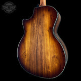 Back view of a wooden acoustic guitar with a dark brown finish on a black background, featuring the Tone Shop logo.