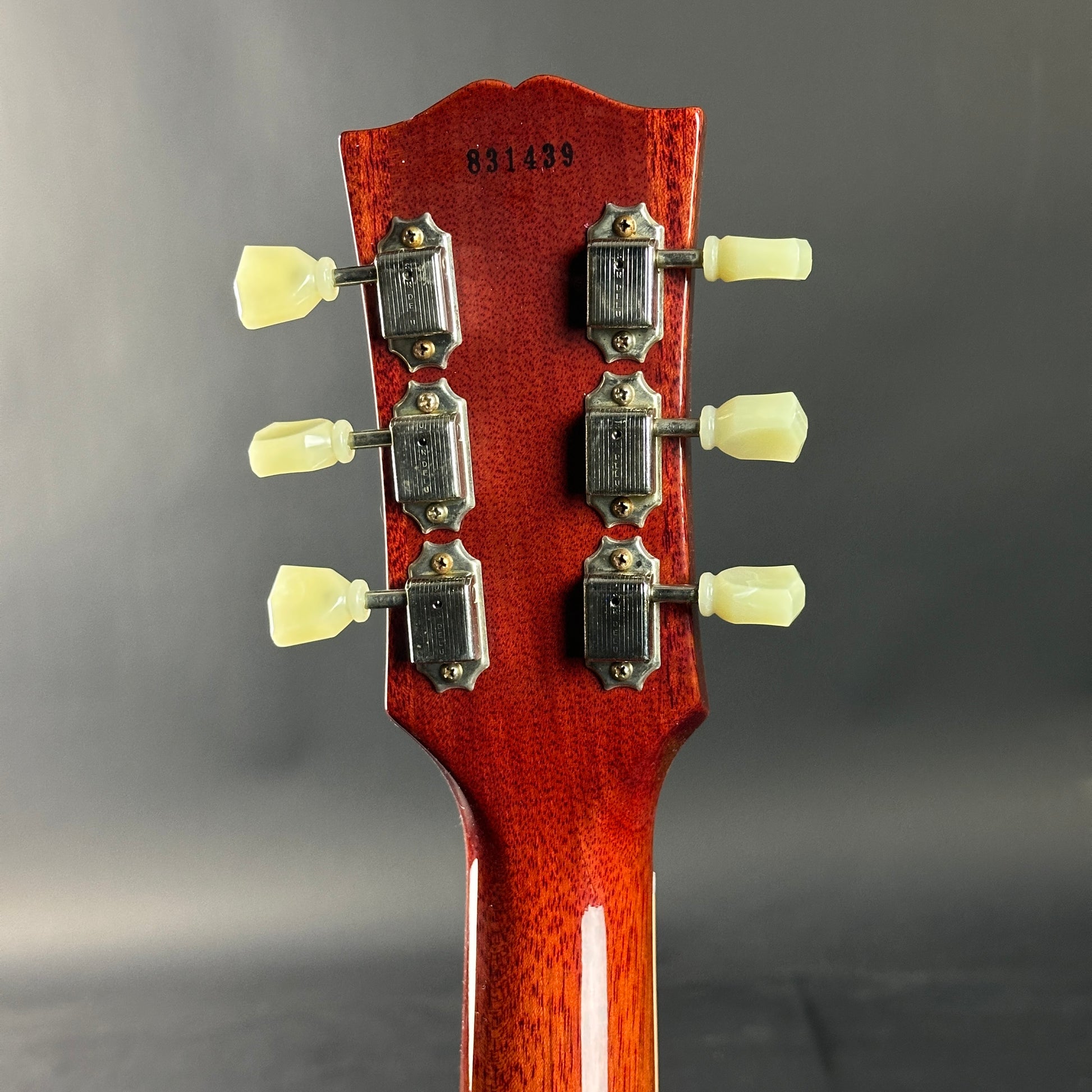 Close-up of a guitar headstock with tuning pegs on a gray background