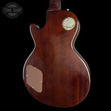 The back of a Gibson Les Paul Custom electric guitar with a glossy dark reddish-brown wood finish, featuring the gold Gibson logo badge and a brown pickguard on a black background.