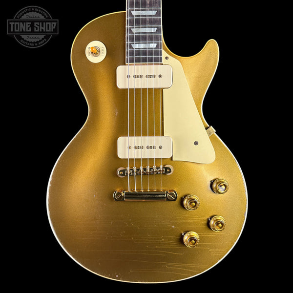 A gold-finish electric guitar with a cream pickguard and white humbucker pickups, shown against a solid black background. A 'Tone Shop' watermark is visible in the top-left corner.