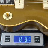 Close-up of the lower bout corner of a gold electric guitar resting on a digital scale displaying 8.7 lbs.