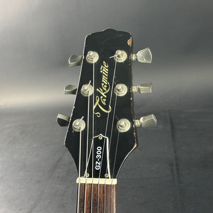 Guitar headstock with Takamine logo and model number on a dark background
