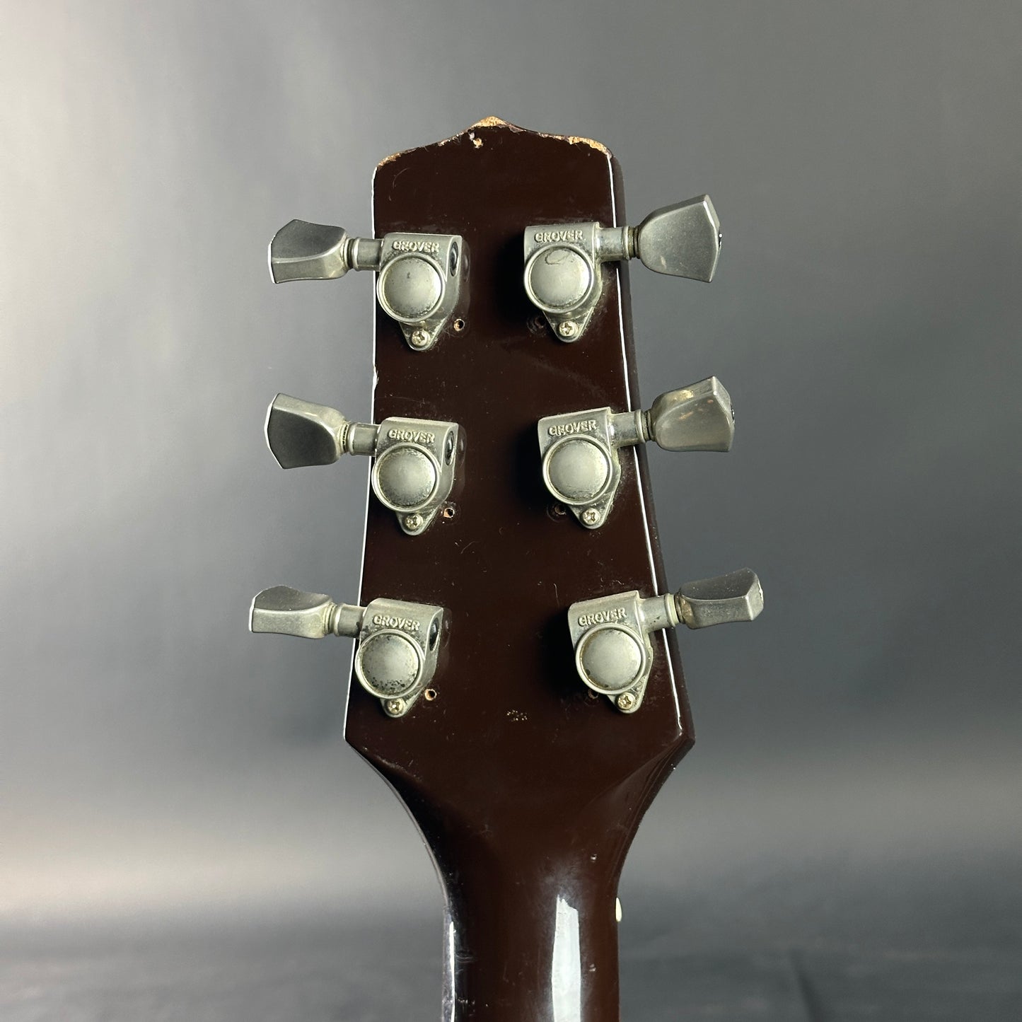 Guitar headstock with tuning pegs on a gray background